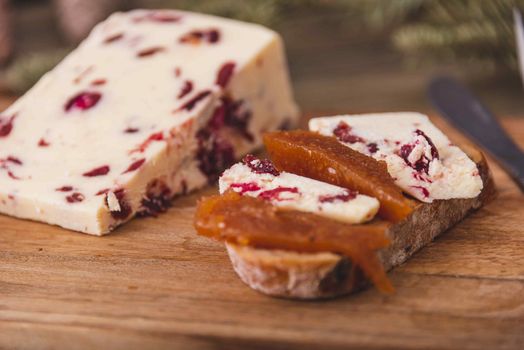 Wensleydale cheese with cranberries, red wine, honey, nuts, raisins on marble cutting board. Black concrete background. Selective focus