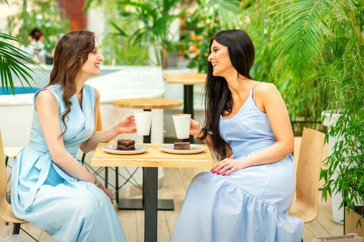 Two beautiful young caucasian smiling women with coffee cups at cafe outdoors
