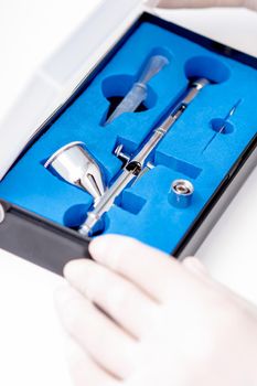 Close up shot of manicure master hand is taking out new clean airbrush tool for nails wearing gloves from the blue box