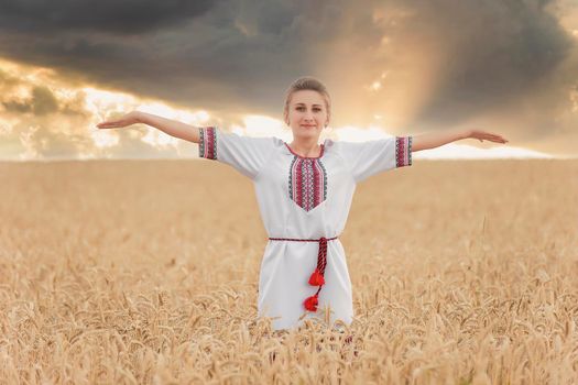 girl in the Ukrainian national costume on the background of a wheat field and sunset sun