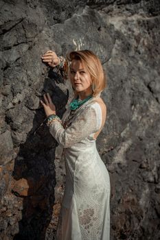 Middle aged woman looks good with blond hair, boho style in white long dress on the beach decorations on her neck and arms