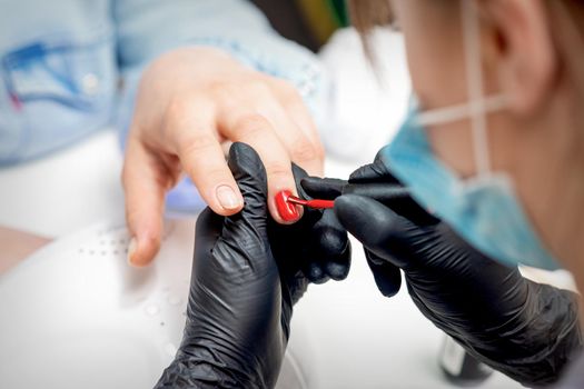 Professional manicure master painting female nails by red nail polish in nail salon