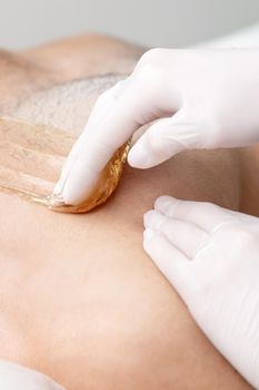 Epilation chest of young male with liquid wax paste by hands of female cosmetologist in beauty salon