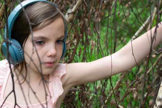 Young beautiful girl fooling around with a branch and wearing headphones on them to listen to music or block out sound due to auditory sensitivity. High quality photo