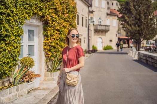 Woman tourist enjoying Colorful street in Old town of Perast on a sunny day, Montenegro. Travel to Montenegro concept. Scenic panorama view of the historic town of Perast at famous Bay of Kotor on a beautiful sunny day with blue sky and clouds in summer, Montenegro, southern Europe.