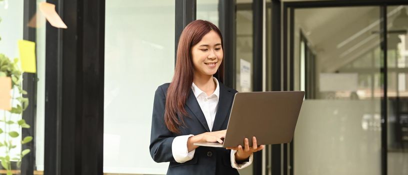 Asian female manager standing in modern office and using computer laptop.