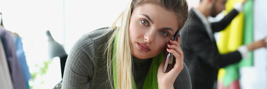 Portrait of blonde creative woman take order on phone for new clothes from client. Popular fashionable atelier with high quality garment. Business concept