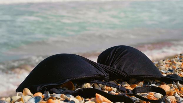 Warm sunny day at the sea, ocean beach. Closeup of bra dumped on sandy beach. Summer vacation concept. Warm day at the seaside.