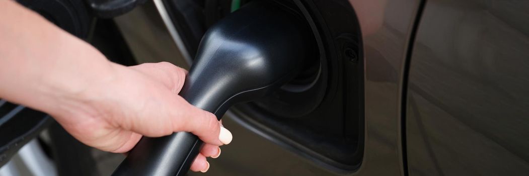 Close-up of woman put fuel nozzle on petrol station to refuel automobile with diesel. Black car on parking or petrol station. Maintenance, vehicle concept