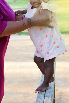 Afro American mom and her cute baby girl's legs, barefoot, on wooden floor. High quality photo