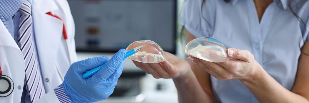 Close-up of professional doctor explain difference between breast implants to client. Medical worker fill patients information for surgery. Beauty concept