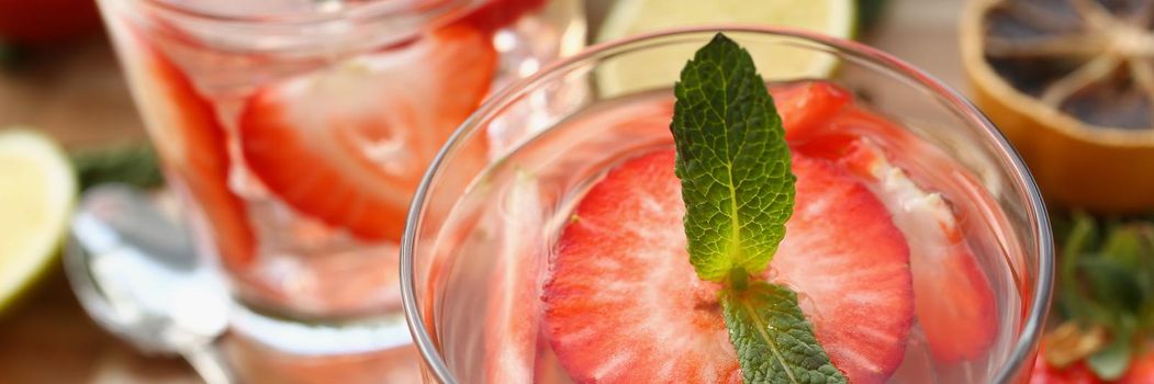 Close-up of glass filled with cooling strawberry cocktail and mint greenery. Fresh slices of fruit in summer time, alcoholic drink. Party. home bar concept