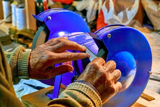 A craftsman who sharpens something. Hands of an elderly man sharpening a knife on a blue grinder.