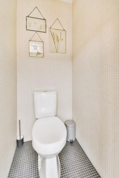 Modern toilet installed on beige wall under button and illuminated shelf in light restroom at home
