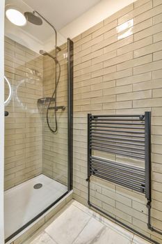 Shower faucets attached to tiled wall near glass partition and ornamental curtail in washroom at home