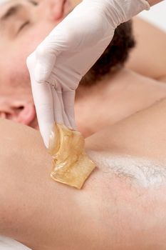 Depilation and epilation male armpit with liquid sugar paste. Hand of cosmetologist applying wax paste on armpit of man. Smooth underarm concept. Out of focus