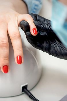 Young woman receives red nail polish by professional manicure master in nail salon