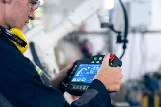 Young factory worker working with adept robotic arm in a workshop . Industry robot programming software for automated manufacturing technology .