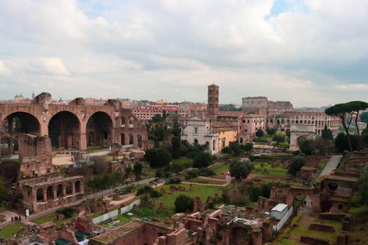 ROME, ITALY - February 05, 2022: Panoramic view around the Colosseum in city of Rome, Italy. Cold and gray sky in the background. Macro photography of the green parks with the old buildings.