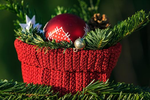 Close-up of a Christmas decoration with a red bauble and fir branches in front of a naturally green background