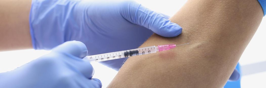 Close-up of nurse injects liquid medication in patient vein with needle. Professional medical worker with cure in syringe. Medicine, clinic, health concept