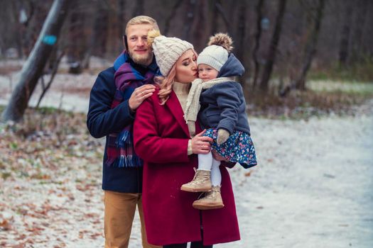 young family with a baby in their arms are walking in the park in winter