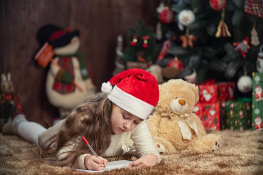 girl writing a letter to santa claus on the background of a decorated christmas tree