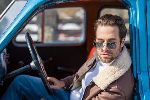 man in sunglasses sits behind the wheel of a retro car
