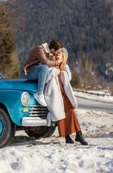 couple kissing near the car on the background of a snowy road