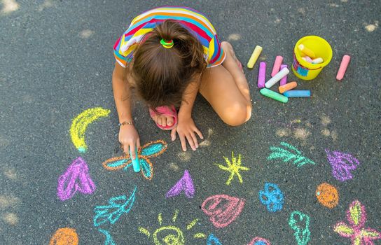 The child draws with chalk on the asphalt. Selective focus. Kids.