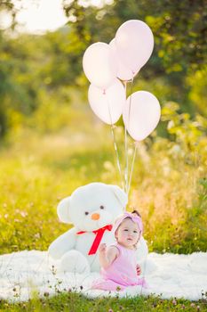 girl sitting in nature with teddy bear and balloons