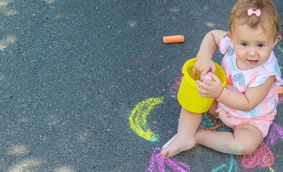 The child draws with chalk on the asphalt. Selective focus. Kids.