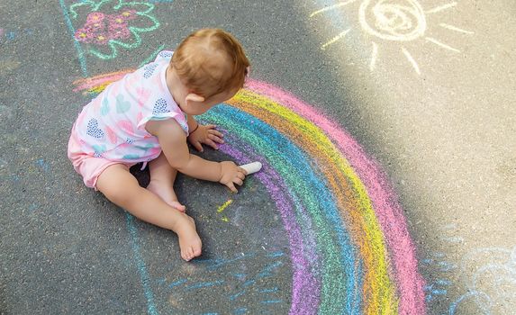 The child draws a house and a rainbow on the asphalt with chalk. Selective focus. Kids.