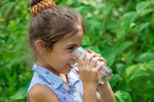 Child girl drinks water from a glass. Selective focus. Kid.