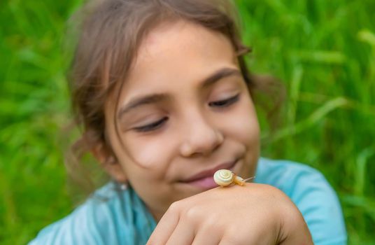 The child looks at the snail through a magnifying glass. Selective focus. Nature.