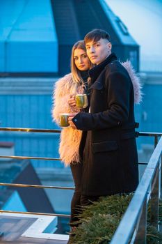 couple with mugs on the terrace of a high-rise building and look at the opening view