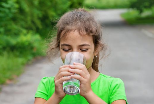 Child girl drinks water from a glass. Selective focus. Kid.