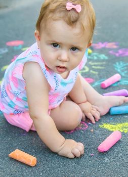 The child draws with chalk on the asphalt. Selective focus. Kids.