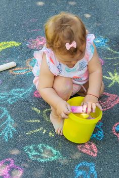 The child draws with chalk on the asphalt. Selective focus. Kids.