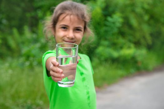 Child girl drinks water from a glass. Selective focus. Kid.