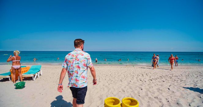Monastir, Tunisia, 2022: Man walking on beach to the sea water, wearing beachwear. Caucasian male enjoying summer, holiday, vacation. Beach with many people on summer season.