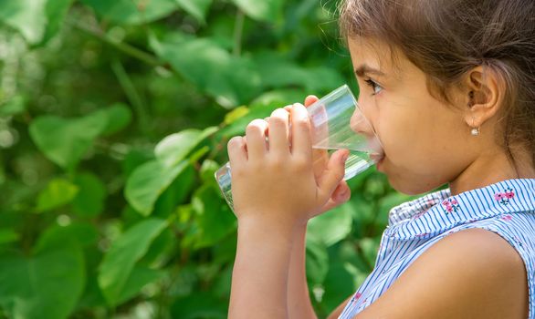 Child girl drinks water from a glass. Selective focus. Kid.