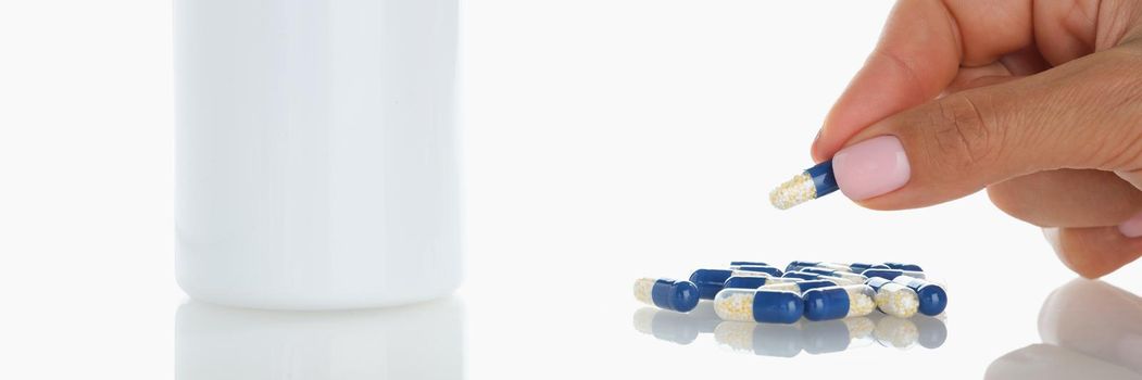 Close-up of female take one blue jelly capsule from bunch on surface. Plastic bottle with meds on table. Healthcare, treatment, recovery, pharmacy concept