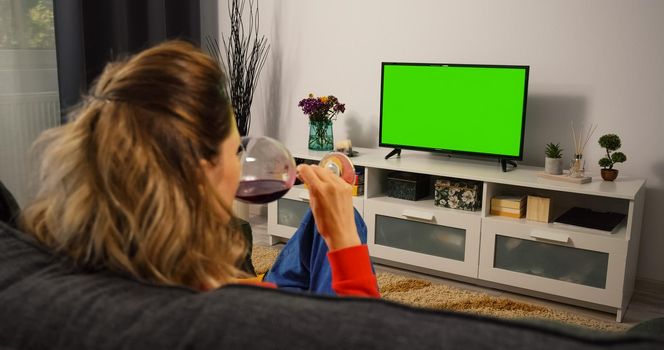 Woman watching Tv Green Chroma Key Screen and Drink wine. Female holds a glass of wine in his hand while watching TV. Relaxing evening.