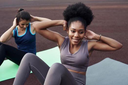 Two young different women go in for sports outdoors in the stadium. ab crunches.