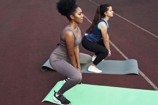 Two female friends do squats with dumbbells outdoors at the stadium