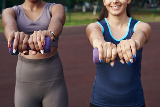 Close up diverse women holding dumbbells and doing exercises outdoors.