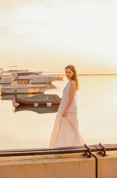 a girl in a white dress stands on the pier against the background of the sea