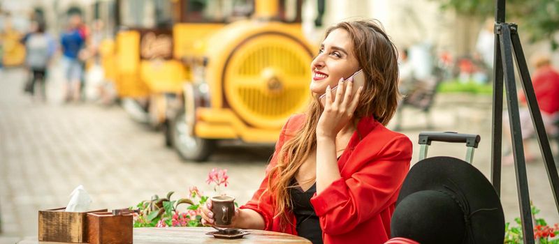 Beautiful happy young caucasian woman talking by cell phone sitting in outdoors cafe at european city