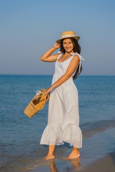 woman in a hat and with a basket in her hands is walking on the beach